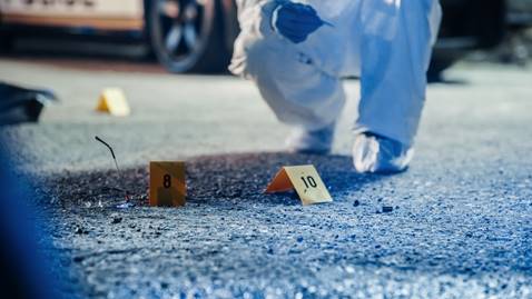 A forensic investigator kneels near evidence markers at a crime scene, with a police car visible in the background. The photo accompanies content about wrongful police shootings.